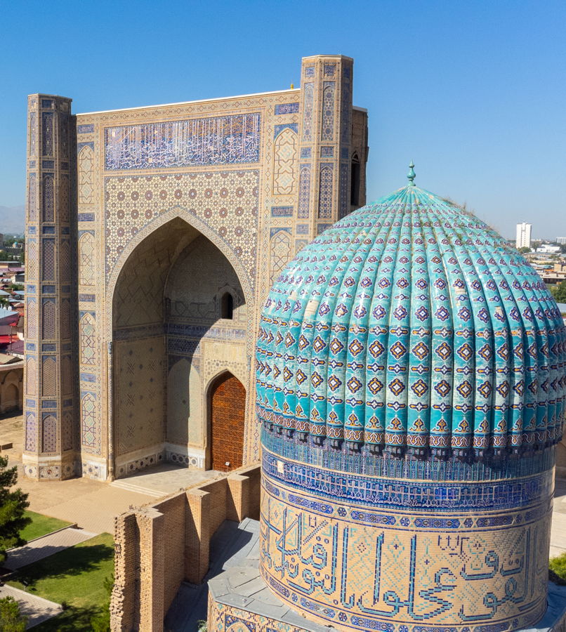 Türkisgeflitterte Kuppel und reich verzierte Portalfassade einer historischen islamischen Medrese mit geometrischen Mosaiken und Kalligrafie.