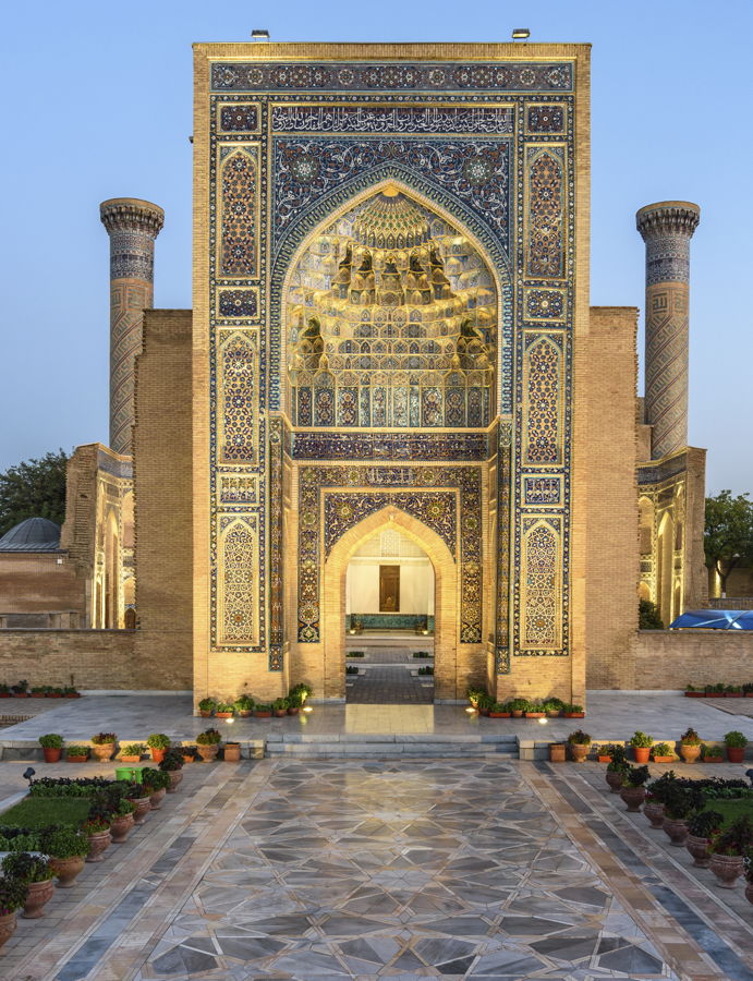 Detailaufnahme der prunkvoll verzierte Eingangsfassade einer historischen islamischen Madrasa mit bunten Fliesen, muqarnas-Portal und hohen Minaretten.
