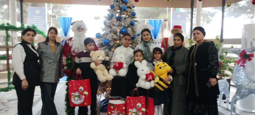 Weihnachts Spendenaktion 2025 Gruppe von Kindern und Erwachsenen vor einem geschmückten Weihnachtsbaum mit Geschenktüten und Plüschtieren