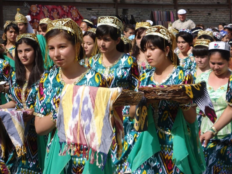 Besuch in Buchara im Rahmen des Projektes «Partnerschaft Junge Frauen in traditionellen, bunten tadschikischen Trachten tragen gewebte Ikat-Tücher auf Körben bei einem folkloristischen Festzug